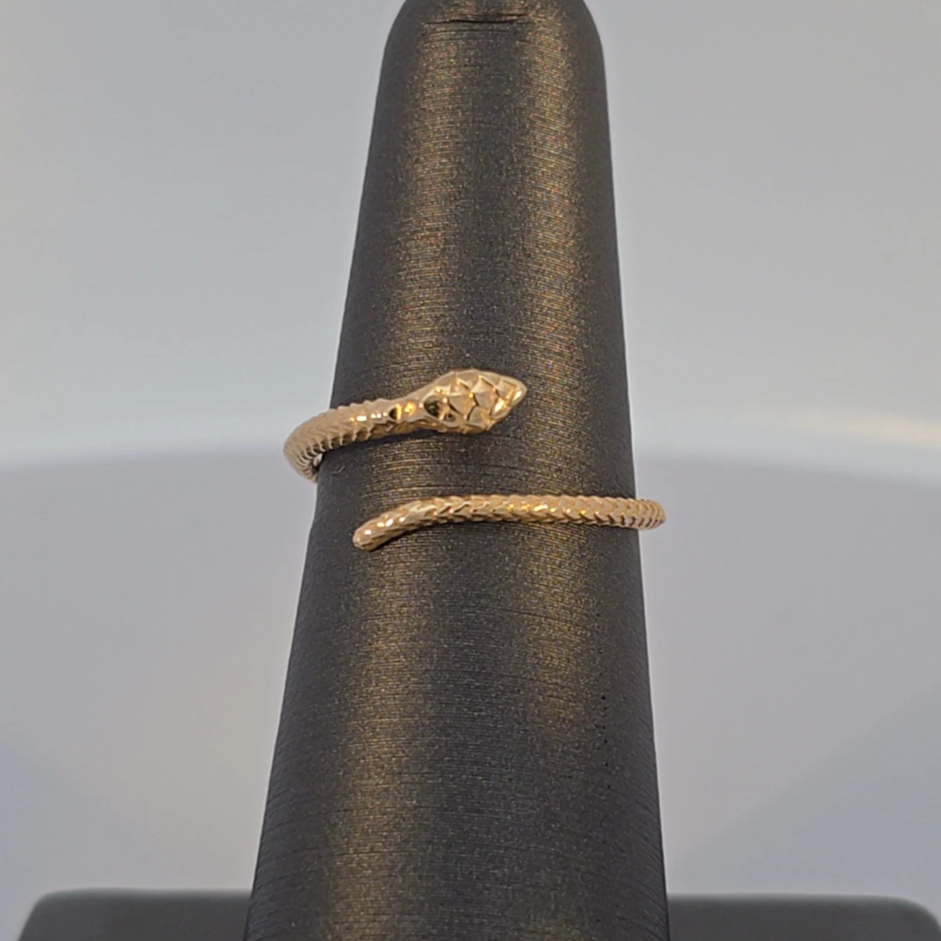 Gold snake-shaped ring on a black ring stand with a gray background